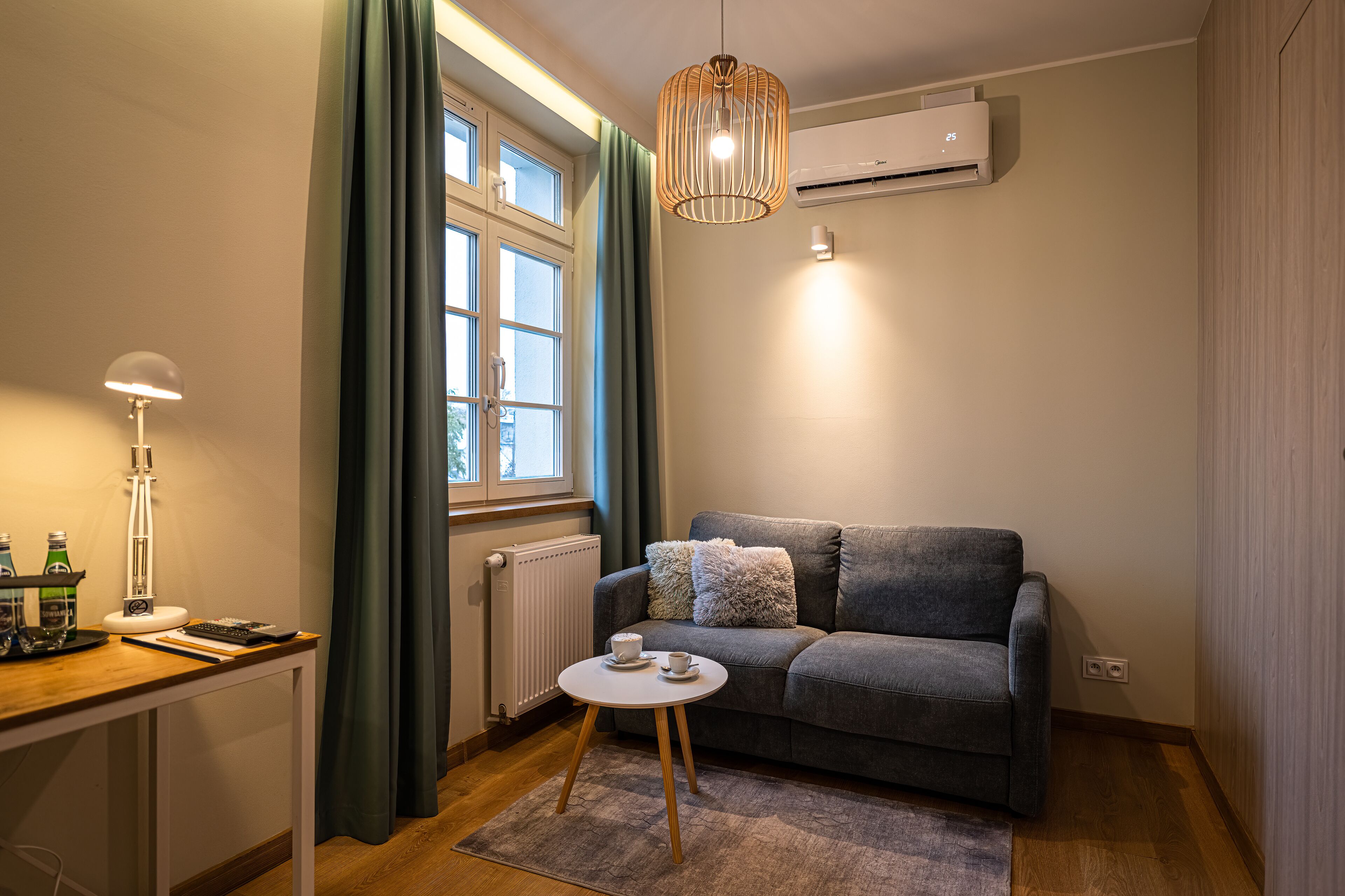 A cozy living area with a sofa, a small round table with a cup and saucer, a lamp, and a window with curtains.