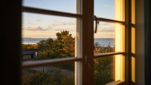 A view through a window with a view of the sea, trees, and a building in the distance. - Villa Bałtycka (Gdansk)