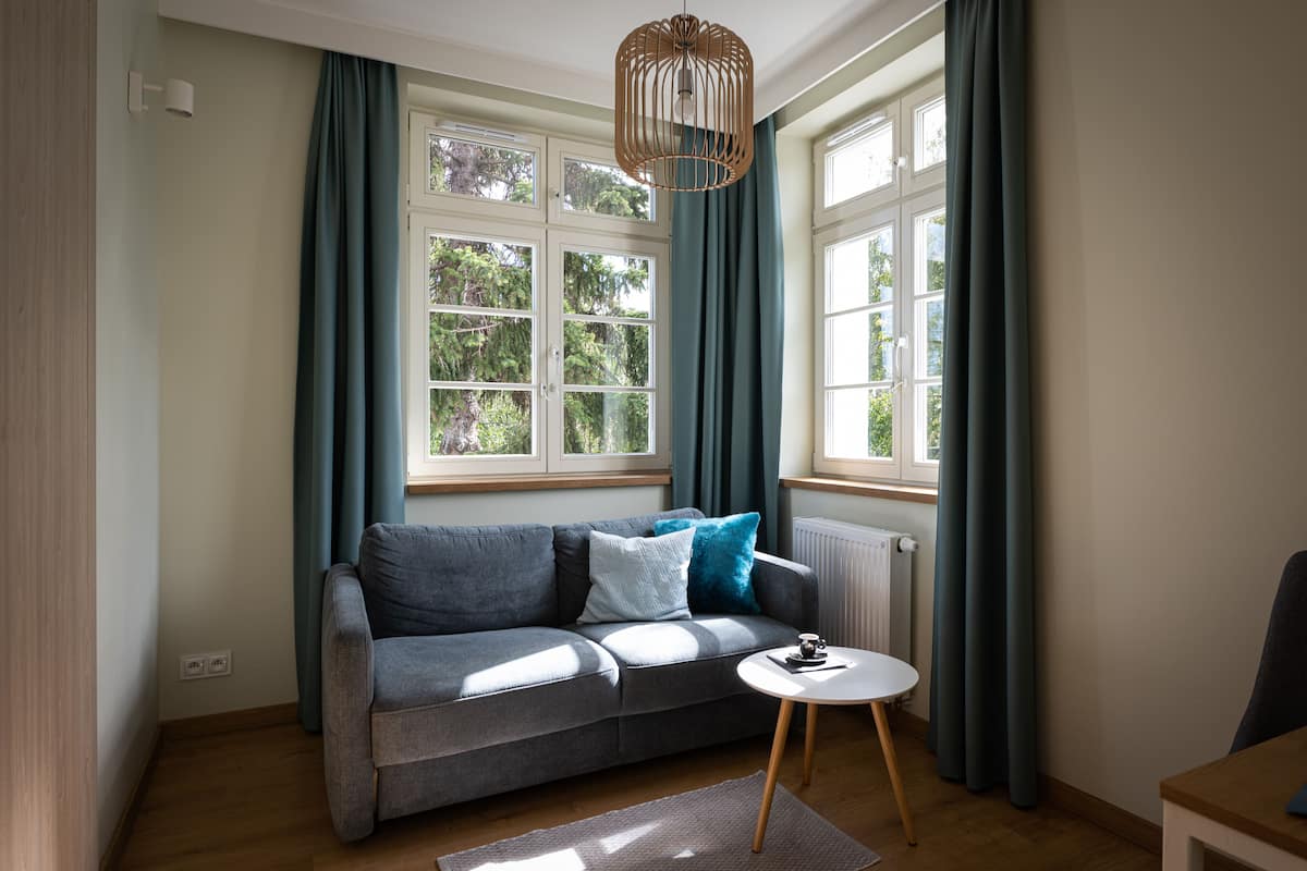 Ein modernes Wohnzimmer mit einem grauen Sofa, einem kleinen runden Tisch und einem Fenster mit Vorhängen.
