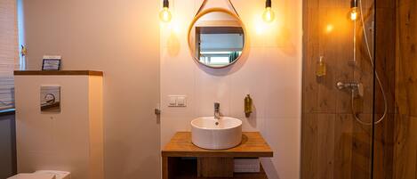 A bathroom with a wooden vanity, a round mirror, a toilet, and a shower area.
