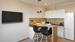 A modern kitchen with a flat-screen TV, wooden countertop, two black chairs, white cabinets, and a white refrigerator. - PaulMarie Apartments on Mayakovskogo 35 (Minsk)