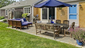 Une terrasse avec une table et des chaises en bois, un parasol bleu et un barbecue.