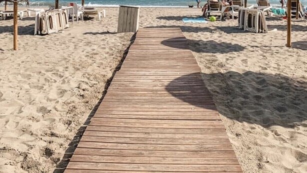 A wooden pathway leading to beach umbrellas and lounge chairs on a sandy beach. - Appartement Palmeras Puerto Paraiso Estepona (Estepona)