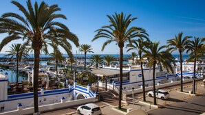 A marina with boats, palm trees, and a white building with blue accents. - Appartement Palmeras Puerto Paraiso Estepona (Estepona)