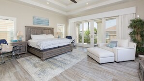 A spacious bedroom with a large bed, a ceiling fan, and a view through the glass doors. - Luxury Home with Theater Room, Private Pool & Beach Views! (South Padre Island)
