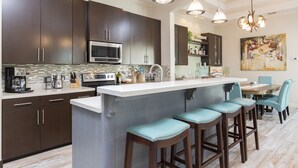 A modern kitchen with dark cabinets, stainless steel appliances, a large island with bar stools, and pendant lighting. - Luxury Home with Theater Room, Private Pool & Beach Views! (South Padre Island)
