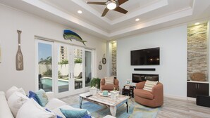 A spacious living room with a white sofa, two armchairs, a coffee table, and a TV mounted on the wall. - Luxury Home with Theater Room, Private Pool & Beach Views! (South Padre Island)