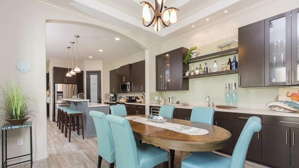 A modern kitchen with dark cabinets, a central island, and a dining area with teal chairs. - Luxury Home with Theater Room, Private Pool & Beach Views! (South Padre Island)