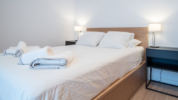 A neatly made bed with white linens and pillows, two bedside tables with lamps, and a wooden headboard.