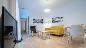 A modern living room with a yellow sofa, white chairs, a small table, and artwork on the walls.