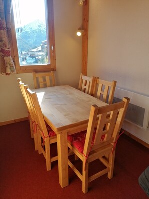 Una mesa de madera para comedor con seis sillas, una ventana con vista a la montaña y un calentador fijado a la pared.