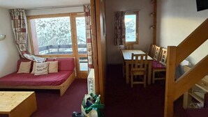 Une pièce confortable avec un lit en bois, une petite table, une table à manger avec des chaises et une fenêtre avec des rideaux.