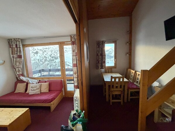 Una habitación acogedora con una cama de madera, una mesita pequeña, una mesa de comedor con sillas y una ventana con cortinas.
