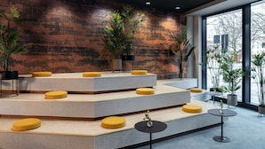 A modern lobby with tiered seating, large windows, and indoor plants. - NH Hannover (Hannover)