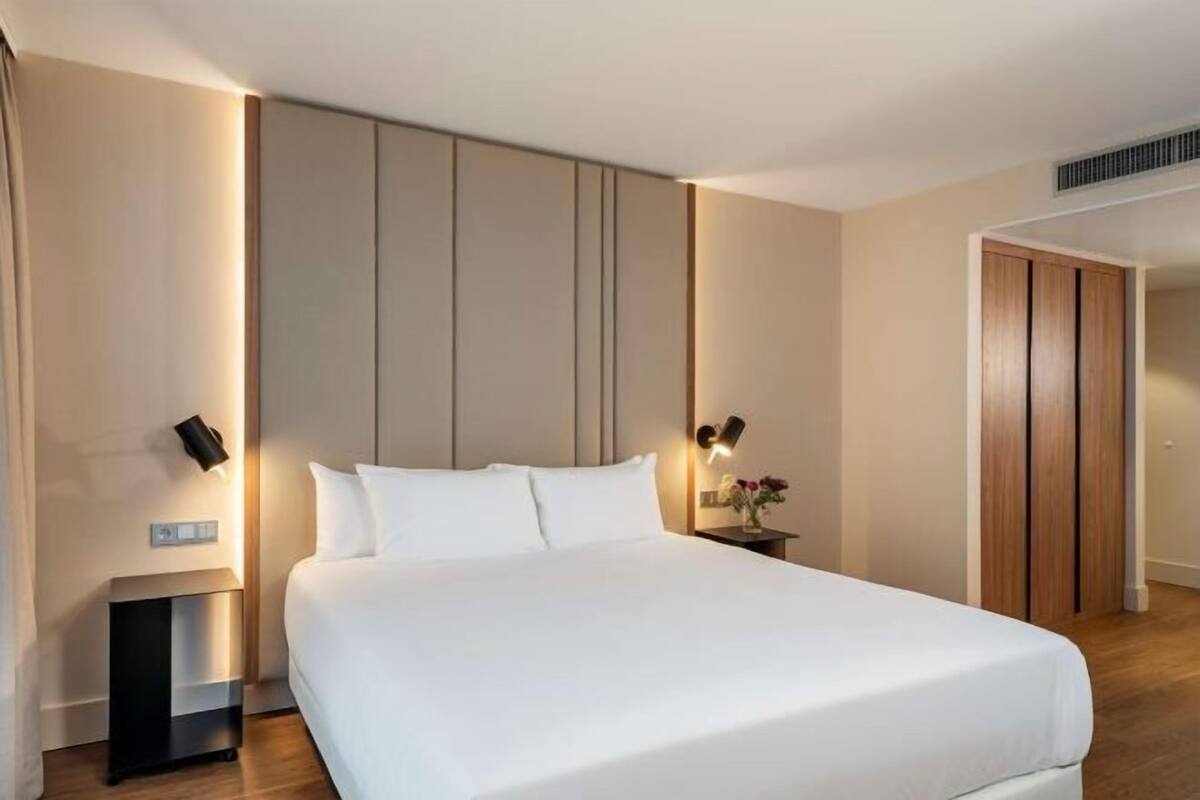 A modern hotel room with a large bed, bedside tables, and a wooden wardrobe.