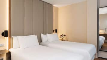 A hotel room with two beds, a bedside table, a wall-mounted light, and a small table with a vase of flowers.