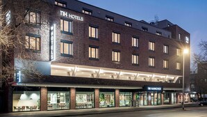 A modern hotel with a brick facade, multiple windows, and a well-lit entrance. - NH Hannover (Hannover)