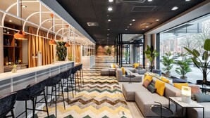 A modern bar area with a long counter, bar stools, and a seating area with sofas and a coffee table. - NH Hannover (Hannover)