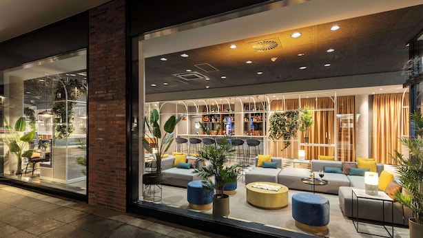 A modern interior with a seating area, a bar, and a large window. - NH Hannover (Hannover)