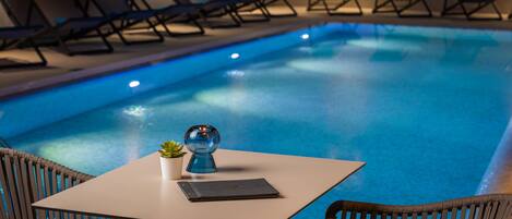 A poolside area with lounge chairs and a table with a plant and a book.