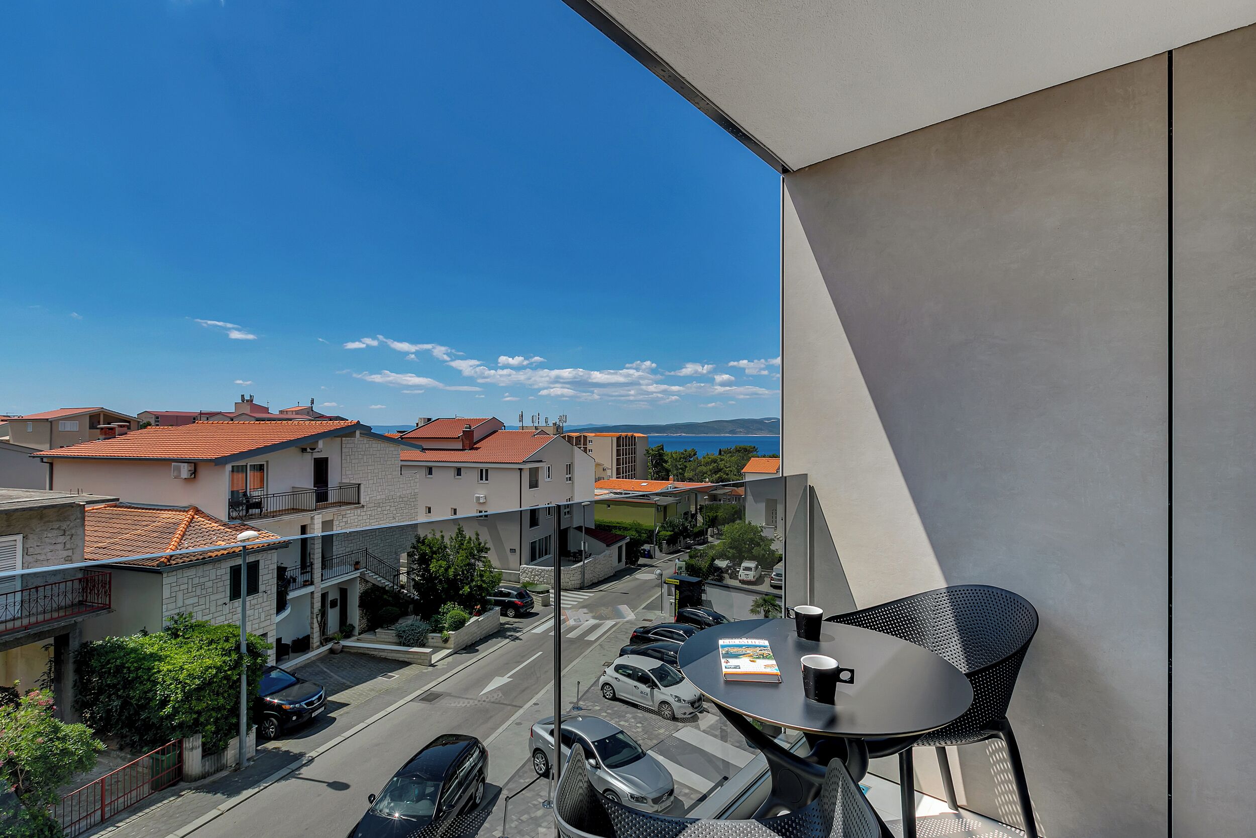 Ein Balkon mit Tisch und Stühlen, der auf eine Straße mit parkenden Autos und Gebäuden blickt.
