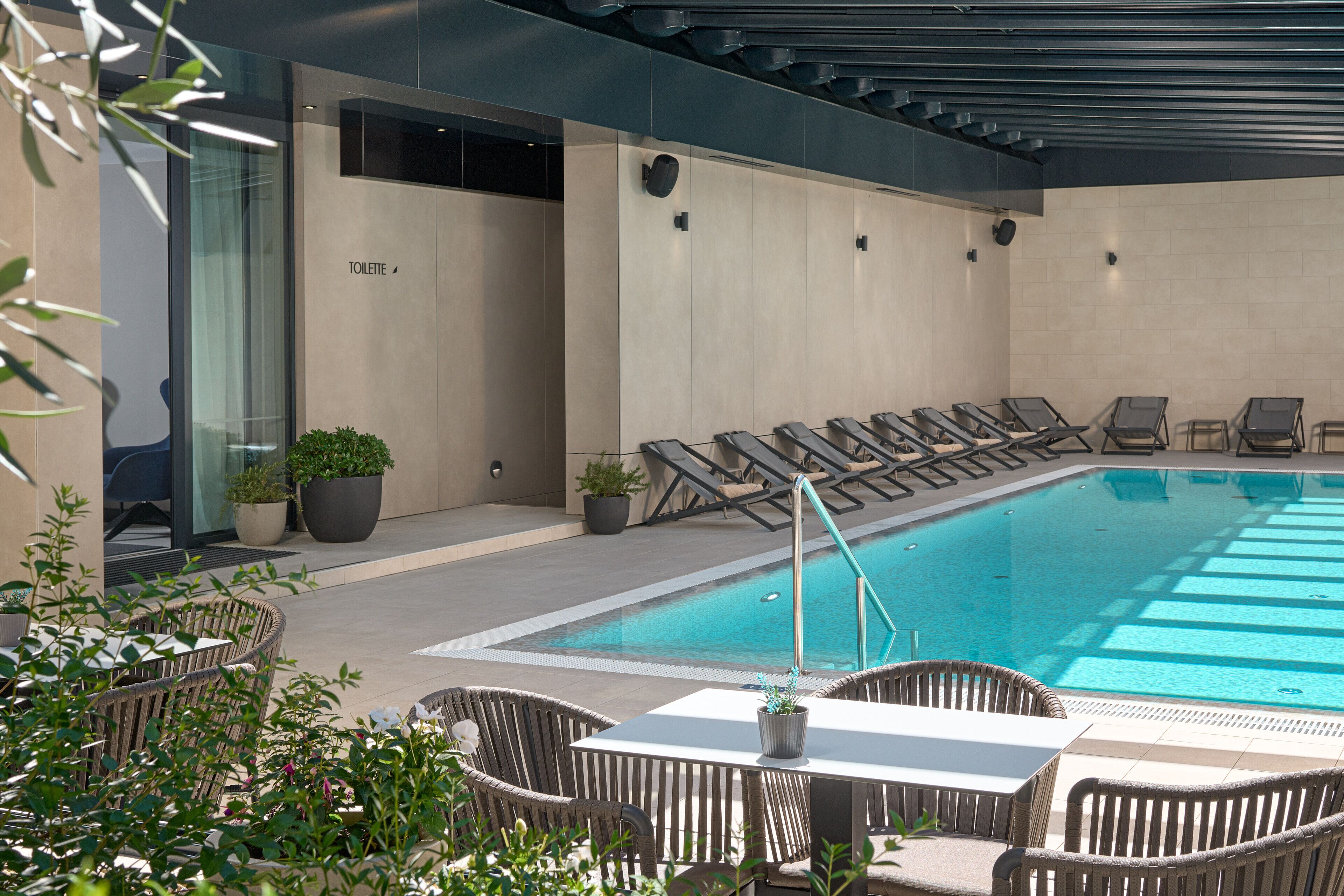 A modern outdoor pool area with lounge chairs and a table, surrounded by potted plants.