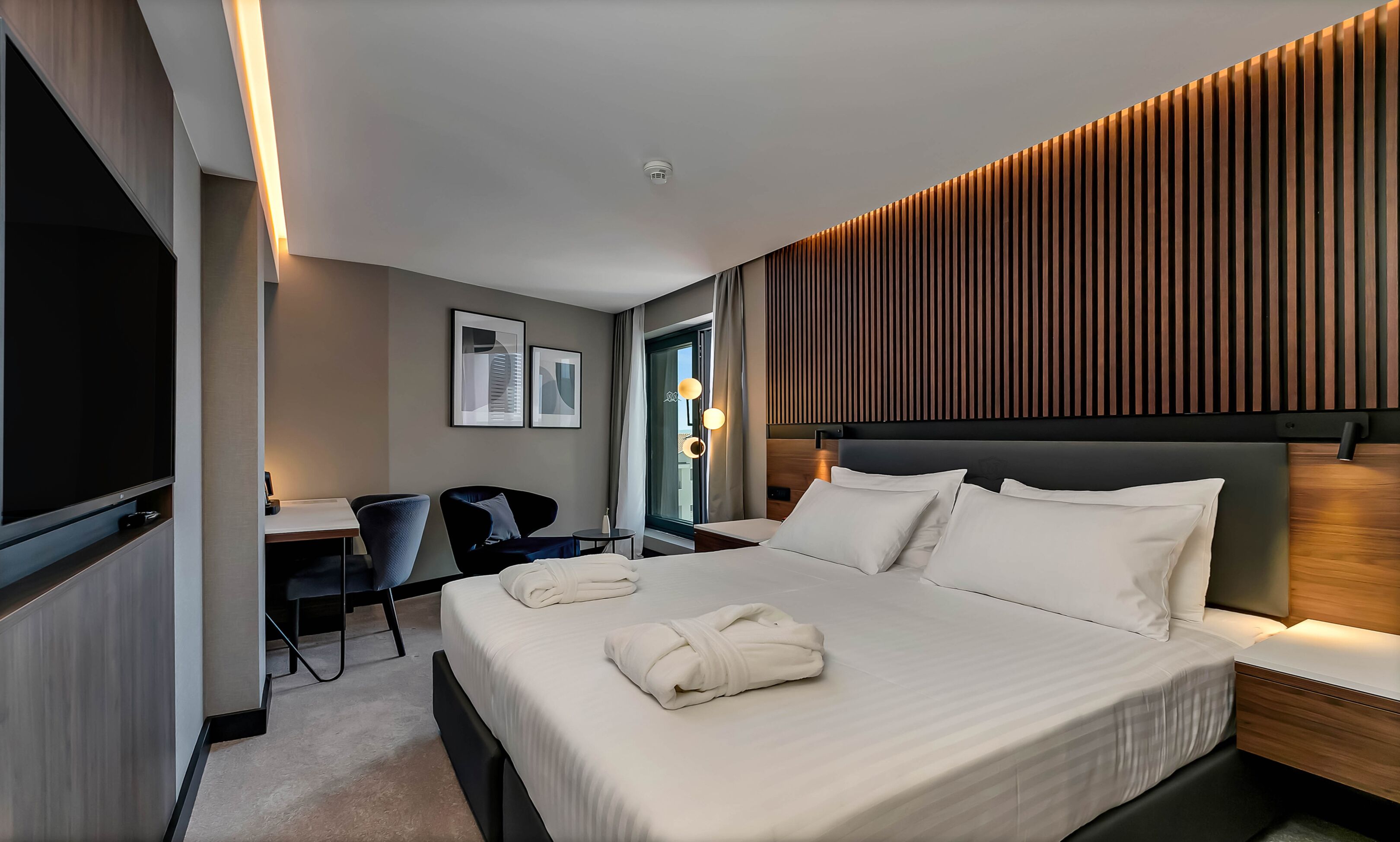 A modern hotel room with a large bed, a desk, and a chair.