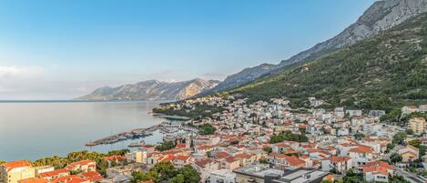 A coastal town with buildings along the waterfront, a marina, and mountains in the background.