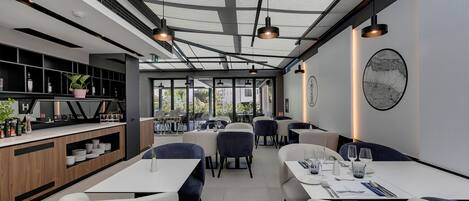 Interior moderno de restaurante con techo alto, vigas a la vista y luz natural proveniente de grandes ventanales.