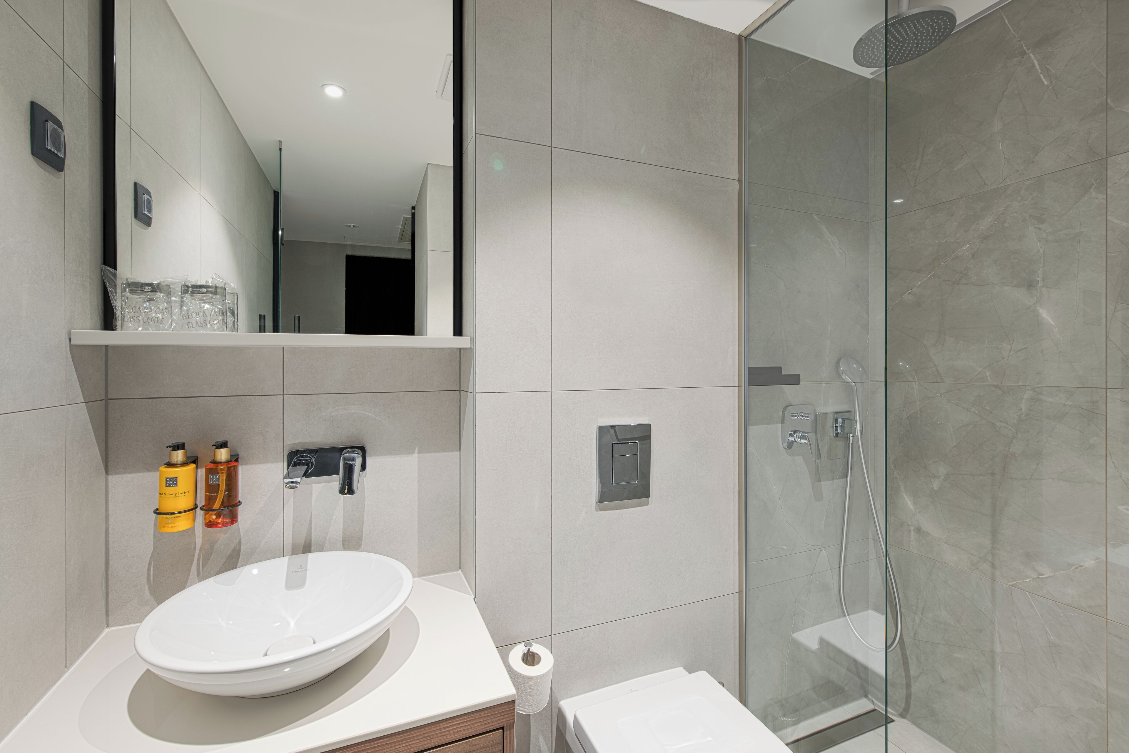 A modern bathroom with a large mirror, a white sink, and a glass-enclosed shower.