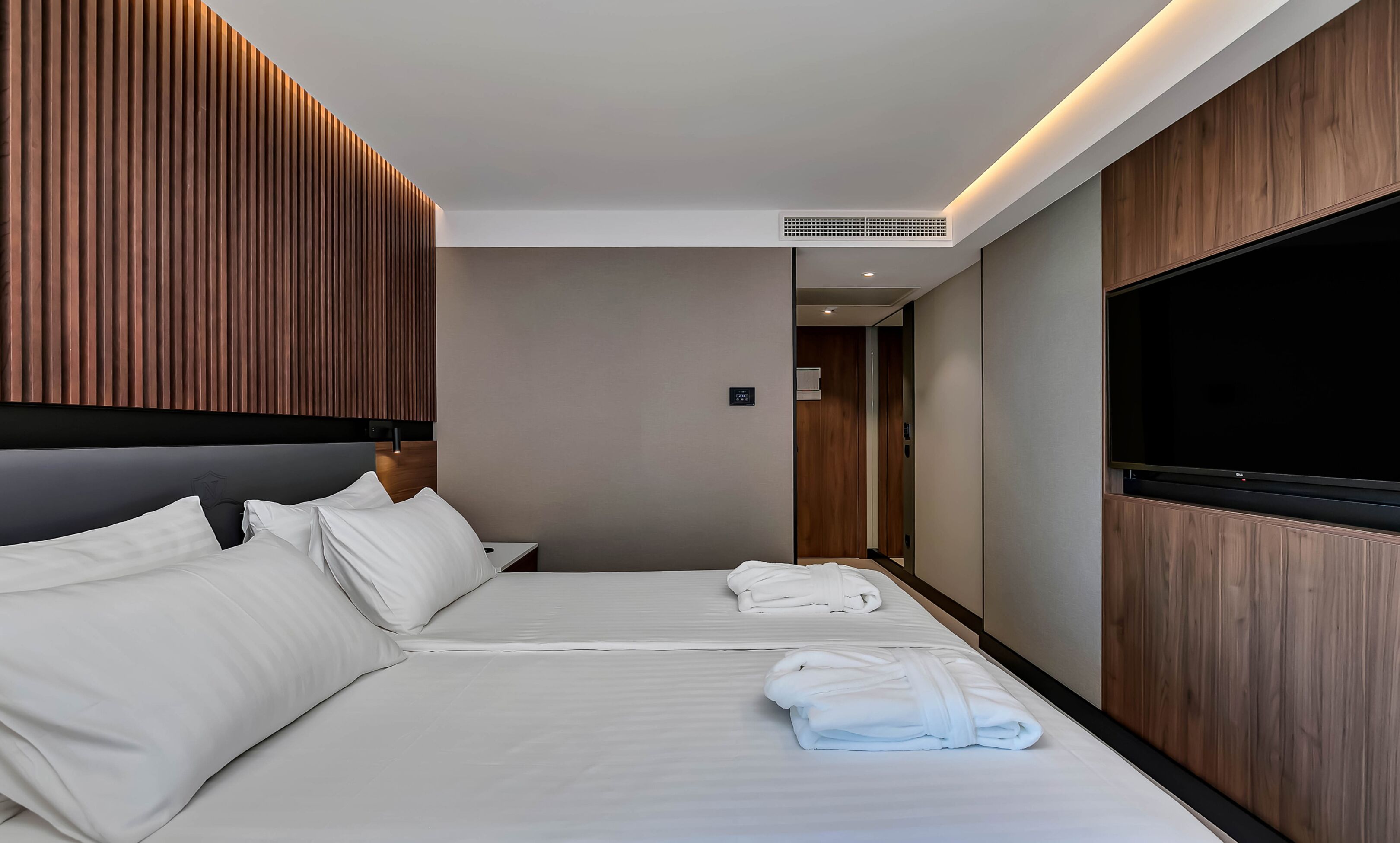 A hotel room with two beds, a flat-screen TV, wooden paneling, and a modern design.