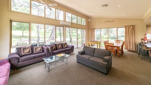 A spacious living room with large windows, a gray sofa, a purple sofa, a glass coffee table, and a dining area with a table and chairs. - "Parkview West" hosted by Halls Gap Accommodation (Halls Gap)
