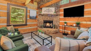 L'intérieur d'une cabane en rondins, avec une cheminée en pierre, des murs en bois, un téléviseur à écran plat et des meubles recouverts d'un tissu vert.