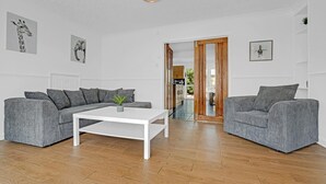 Ein modernes Wohnzimmer mit einer grauen Sofagarnitur, einem weißen Couchtisch und einem Holzboden.