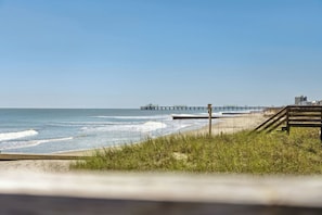 Ein Strand mit einer Holzpromenade, die zu einem Steg führt, der ins Meer hinausragt.