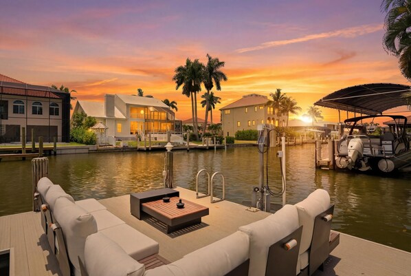 A waterfront property with a dock, lounge area, and buildings with a sunset view.