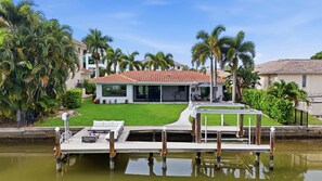 A house with a red-tiled roof, a covered patio, and a dock extending into a body of water.
