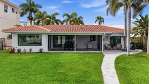 A modern house with a tiled roof, large windows, a patio with outdoor furniture, and a well-maintained lawn. - Sunset Dock Pet-Friendly & Steps to Beach (Naples)