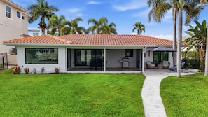 A modern house with a tiled roof, large windows, a patio with outdoor furniture, and a well-maintained lawn.