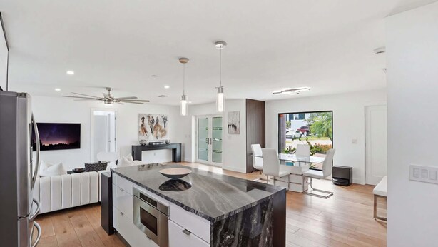 A modern kitchen with a central island, a dining area with a table and chairs, and a view of the outdoors. - Sunset Dock Pet-Friendly & Steps to Beach (Naples)