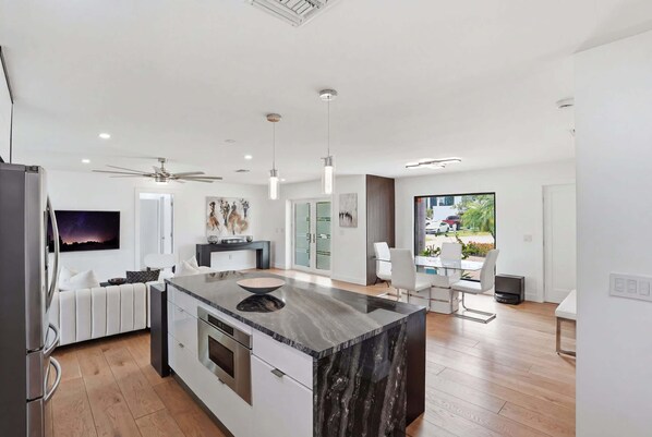 A modern kitchen with a central island, a dining area with a table and chairs, and a view of the outdoors.