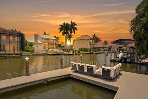 A waterfront hotel with a dock, lounge chairs, and a sunset view.