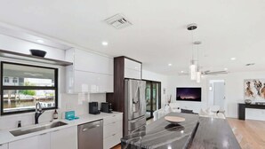 A modern kitchen with white cabinetry, stainless steel appliances, a large window, and a dining area with a marble island. - Sunset Dock Pet-Friendly & Steps to Beach (Naples)