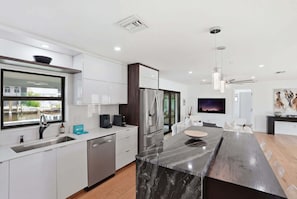 A modern kitchen with white cabinetry, stainless steel appliances, a large window, and a dining area with a marble island.