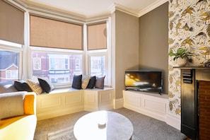 A living room with a bay window, a flat-screen TV, a fireplace, and a sofa.