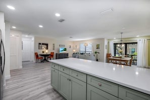 A modern kitchen with a large island, a dining area with a table and chairs, and a living room with a sofa and TV.