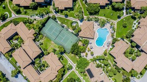 Vue aérienne d’un quartier résidentiel avec un court de tennis, une piscine et des maisons à l’architecture similaire.