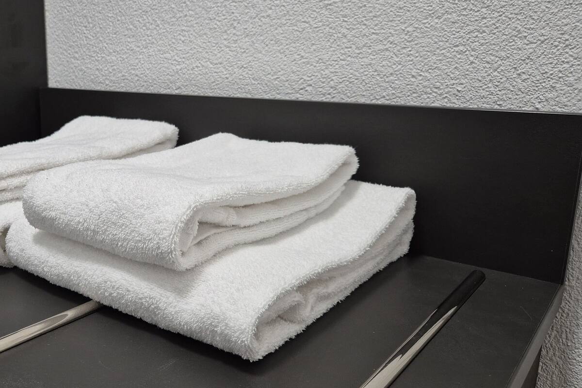 A stack of white towels on a metallic surface in a room with a textured wall.