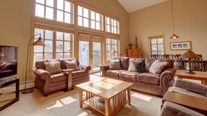 A spacious living room with large windows, leather sofas, a wooden coffee table, and a television. - Largest Condo In Passage Point, Vaulted Ceilings, Huge Balcony - PP514 by Redawning (Copper Mountain)