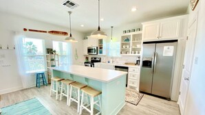 A modern kitchen with a central island, bar stools, white cabinetry, and a stainless steel refrigerator.